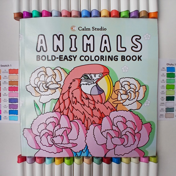 Illustration of the cover of a coloring book, featuring a majestic macaw perched among branches adorned with blooming carnations.